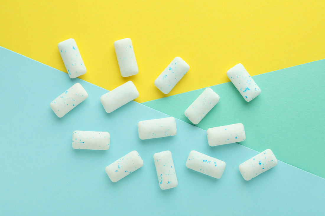 White chewing gum pieces on a yellow and blue pastel background, highlighting oral health benefits.