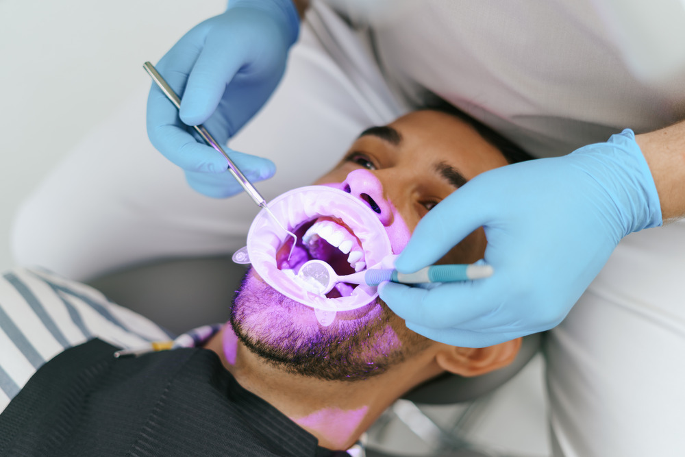 Cosmetic dentistry in Mohali A patient undergoing professional teeth whitening treatment at a cosmetic dentistry clinic, with dental tools and protective equipment used by the dentist.