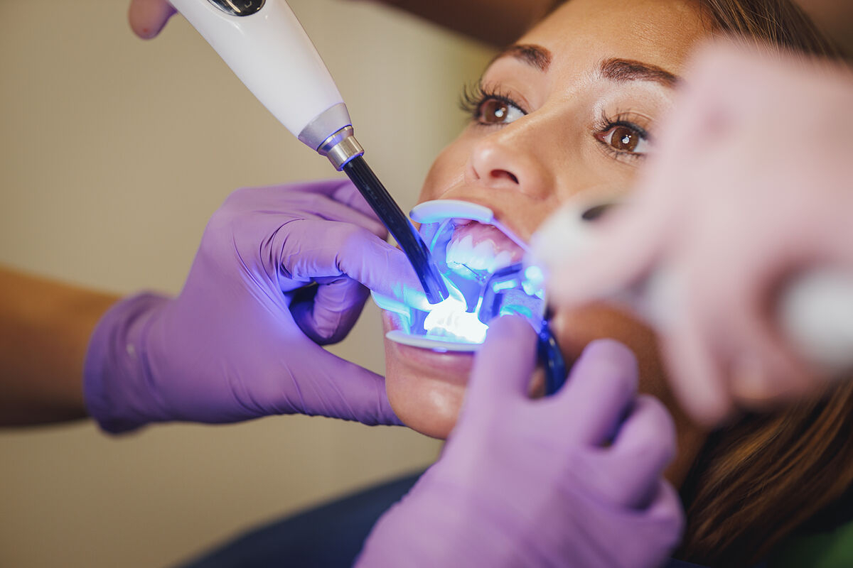 A woman receiving professional teeth whitening treatment with LED light technology at a cosmetic dentistry clinic.